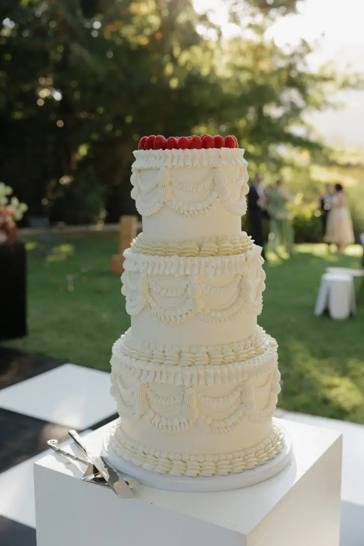 Three-tier off-white wedding cake with vintage lambeth style decorations, topped with raspberries - by Crumb Boutique Bakery, Cape Town